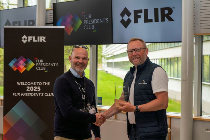 David Atkins accepts a glass President's Club award from FLIR's David Mills. In the background are FLIR and FLIR President's Club branding and banners. 