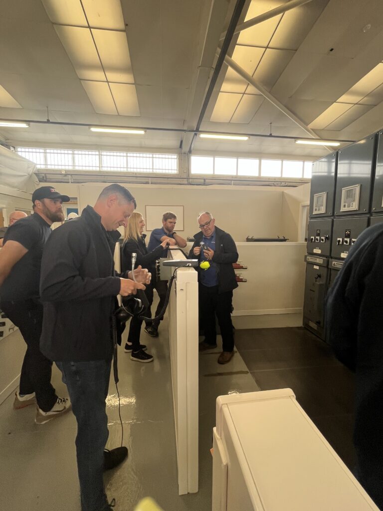 Attendees stand around PASS' mock substations taking notes and measurements using EA Technology's UltraTEV Plus 2 tools.