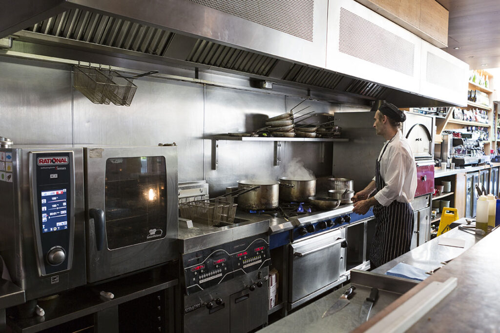 Commercial catering kitchen with male chef cooking at the hob. 