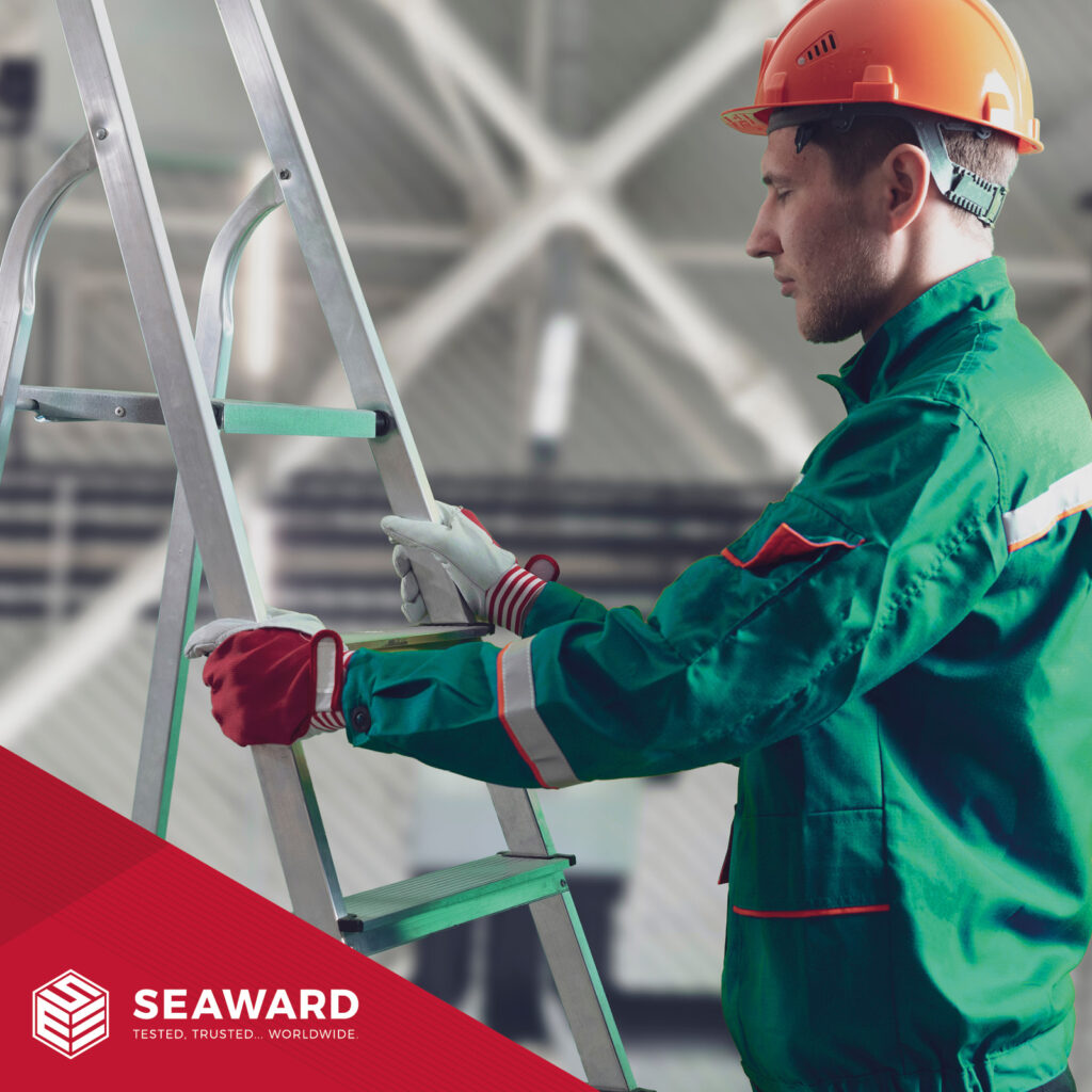 A man in a green work jacket and orange hardhat holds onto a silver ladder. Seaward's logo is in the bottom left of the image. The logo is on a red background. 