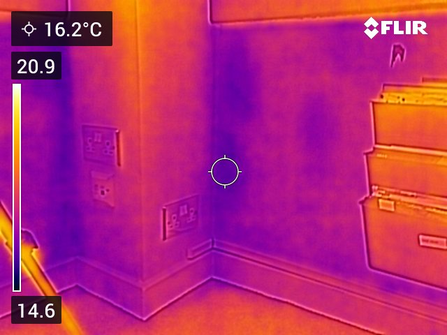 Thermal image of an office wall. There are cold patches in the corners and various points across the wall. 
