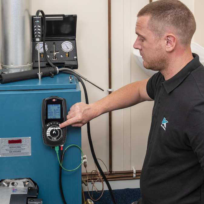 A man in a Black Kane polo shirt is  testing a boiler using a Kane 958 Flue Gas Analyser. 