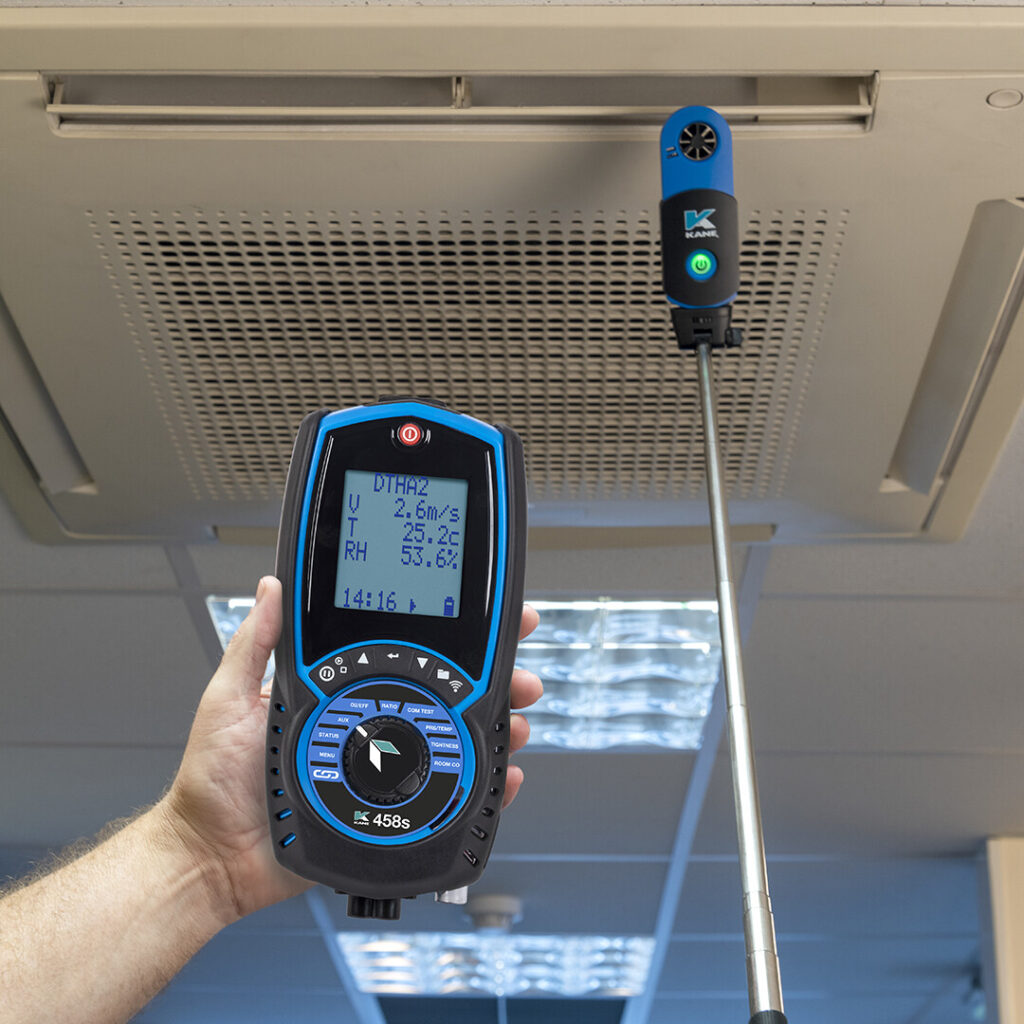 A hand holds a Kane 458 Flue Gas Analyser while a Kane DTHA2 Wireless Airflow, Temperature & Humidity Adapter is held to an vent using a long probe stick. 