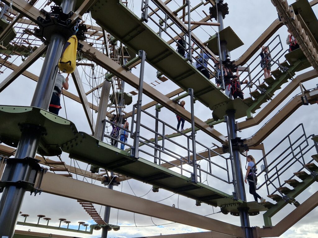 Photo taken beneath the air trail. Various people in harness are dotted about the large climbing structure. 