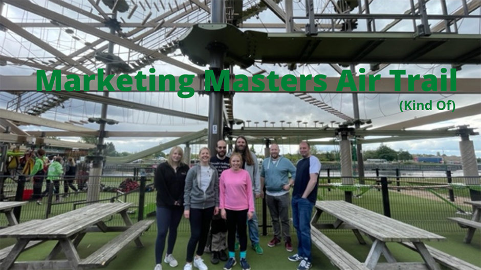 Members of the marketing department pose under the Air Trail for a photo. Above them large green text reads 'Marketing Masters Air Trail'; under this heading smaller green text reads '(Kind Of)'. 