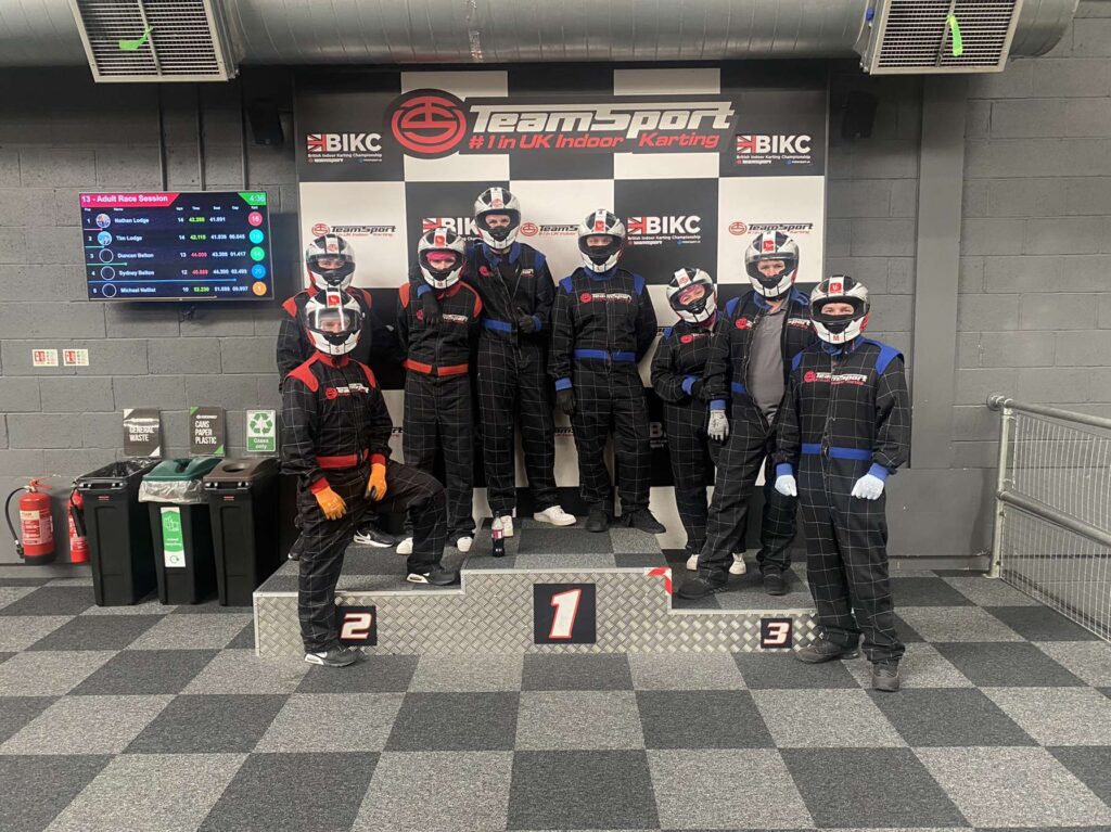 Eight members of the calibration team pose in black and red/blue jumpsuits on a racing podium. 