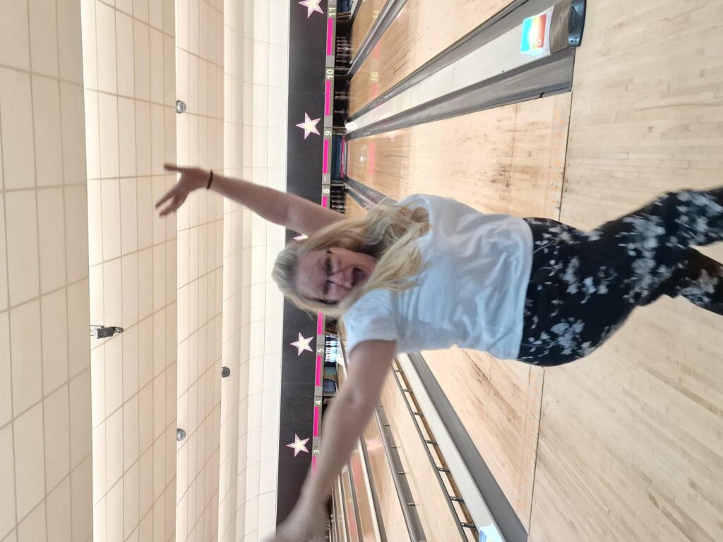 Claire celebrates getting a strike with her hands in the air.