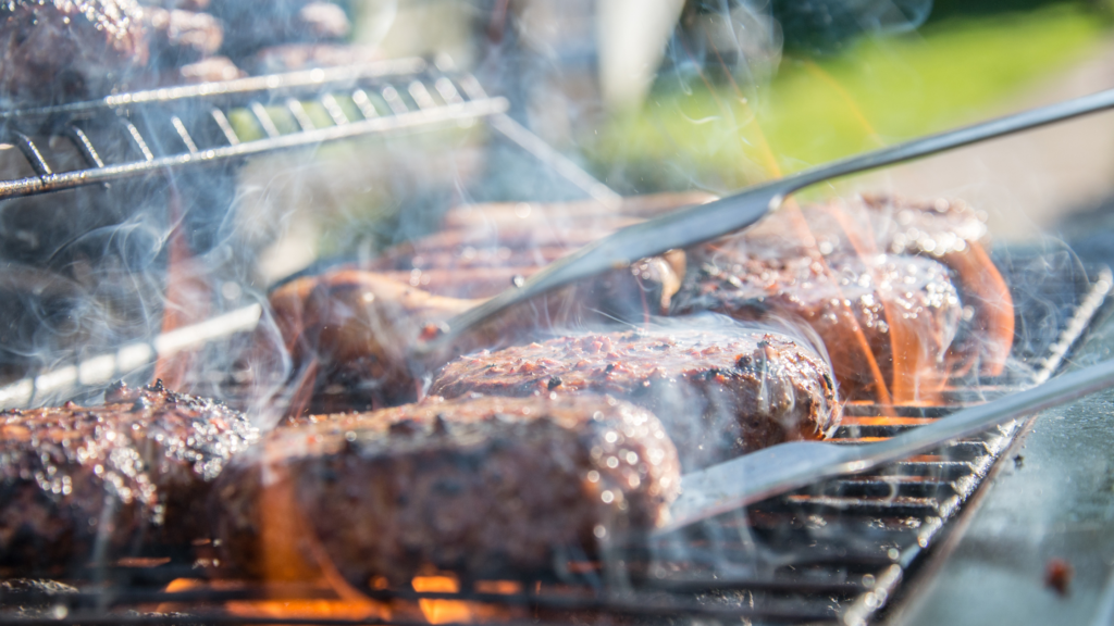 Burgers are being cooked on a barbeque. 