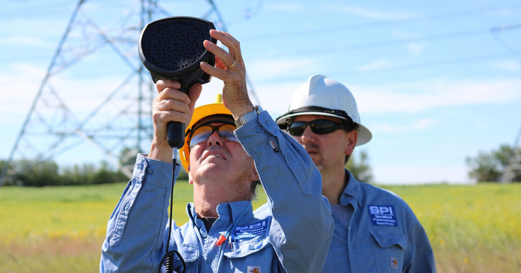 Two male SPI employees in hardhats are using the FLIR Si124 Acoustic Imager to inspect electricity lines. 