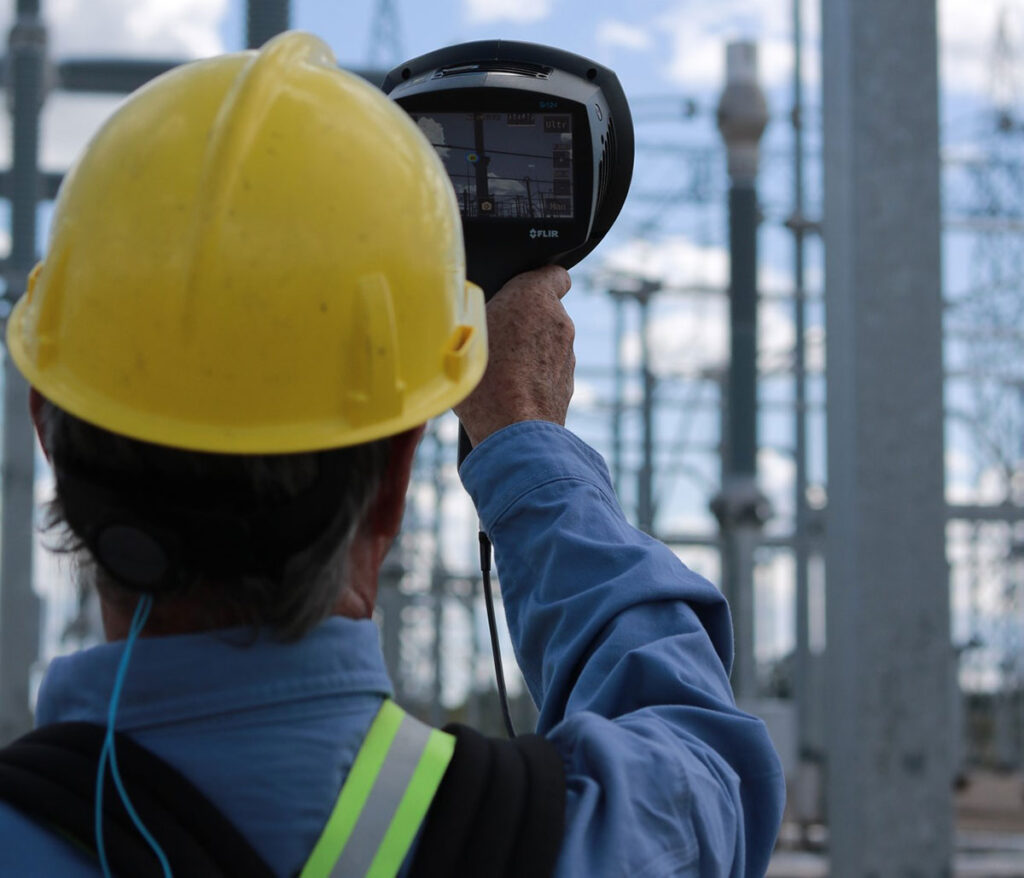 A man in a hardhat is using the FLIR Si124 Acoustic Imager to inspect a power plant. 