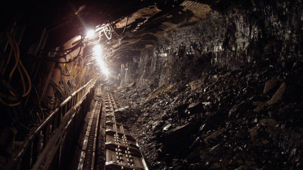 The inside of a mine with a track in the middle. Lights on the left side of the mine illuminate the channel. 