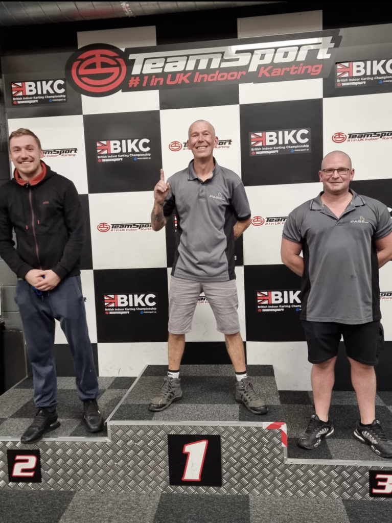 Three members of the Dispatch team stand on the podium. Phil stands on 3rd place, Arturs in 2nd place, and Lee, the winner, stands on top of the podium in 1sty place. 