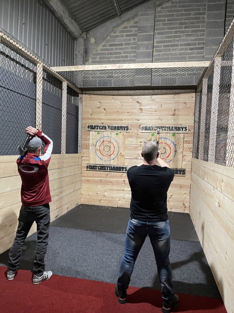 Two members of the dispatch team stand ready to throw axes at wooden targets on the wall opposite. 