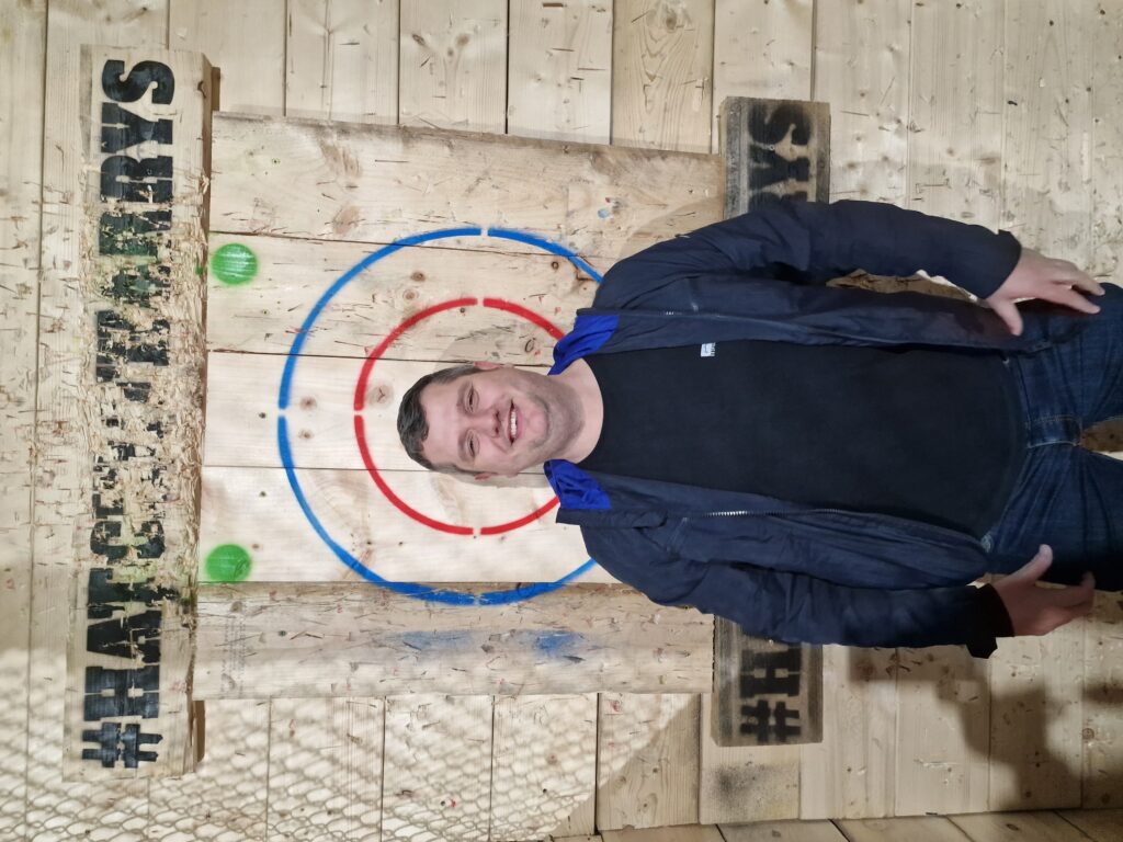 Gary stands in front of a wooden axe-throwing target. 