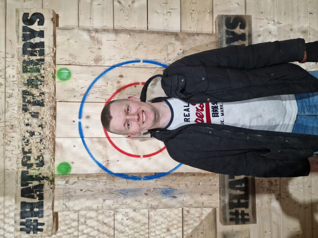 Lewis stands in front of a wooden axe-throwing target. 