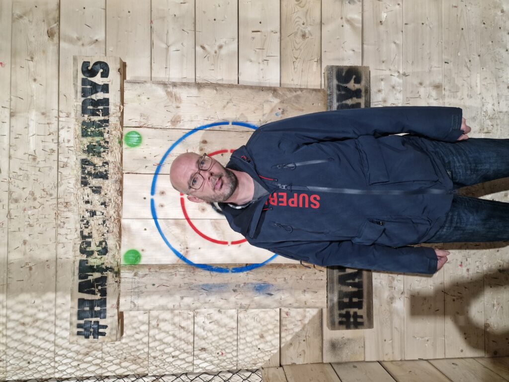 Stephen stands in front of a wooden axe-throwing target. 