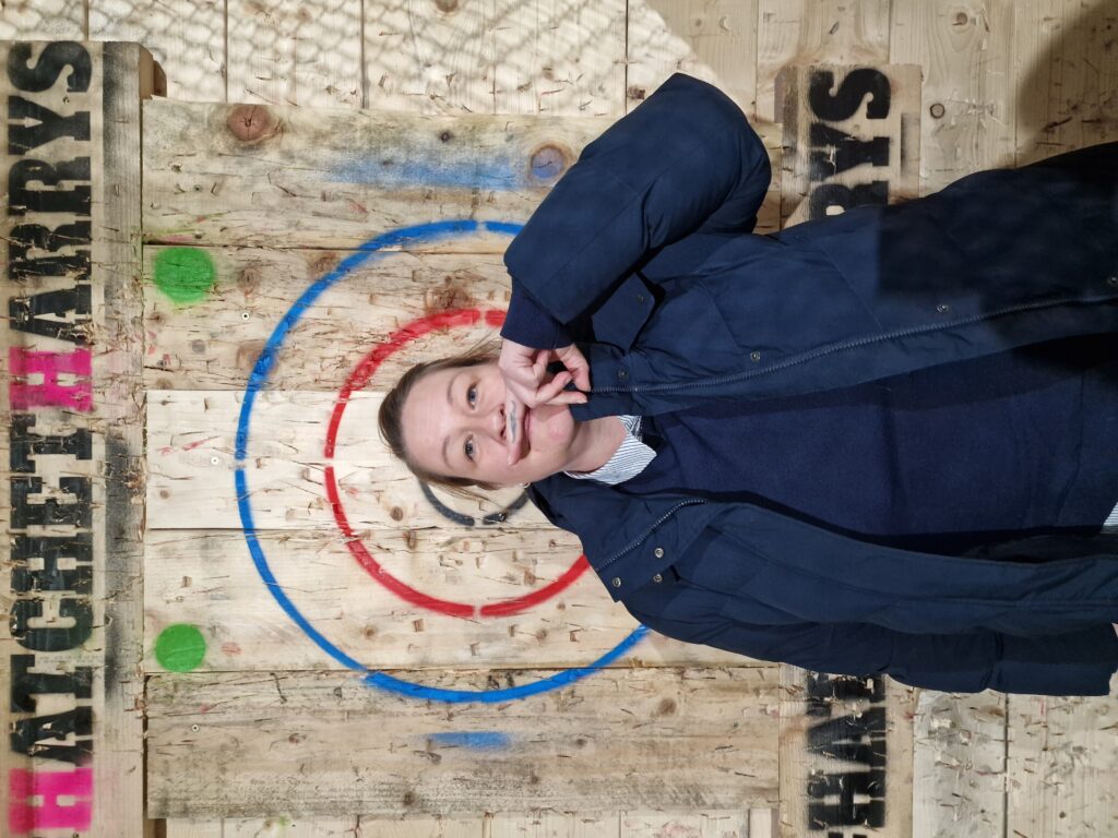 Sally stands in front of a wooden axe-throwing target. 