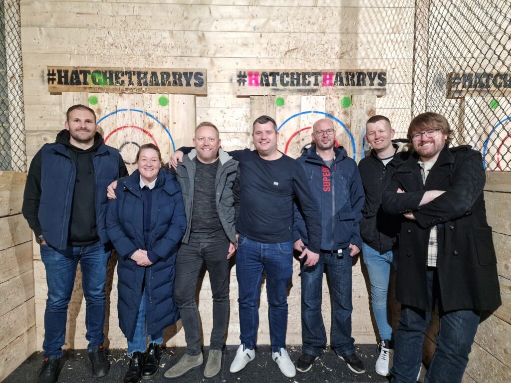 Image of the Sales Team standing in front of two wooden axe-throwing targets. From left to right: Chris M, Sally, David, Gary, Stephen, Lewis, Chris C.
