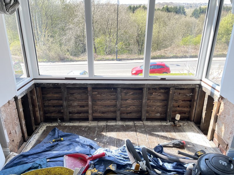 Digital image of the inside of a bay window. The wall at the bottom of the window has been pulled away to reveal the wood behind.