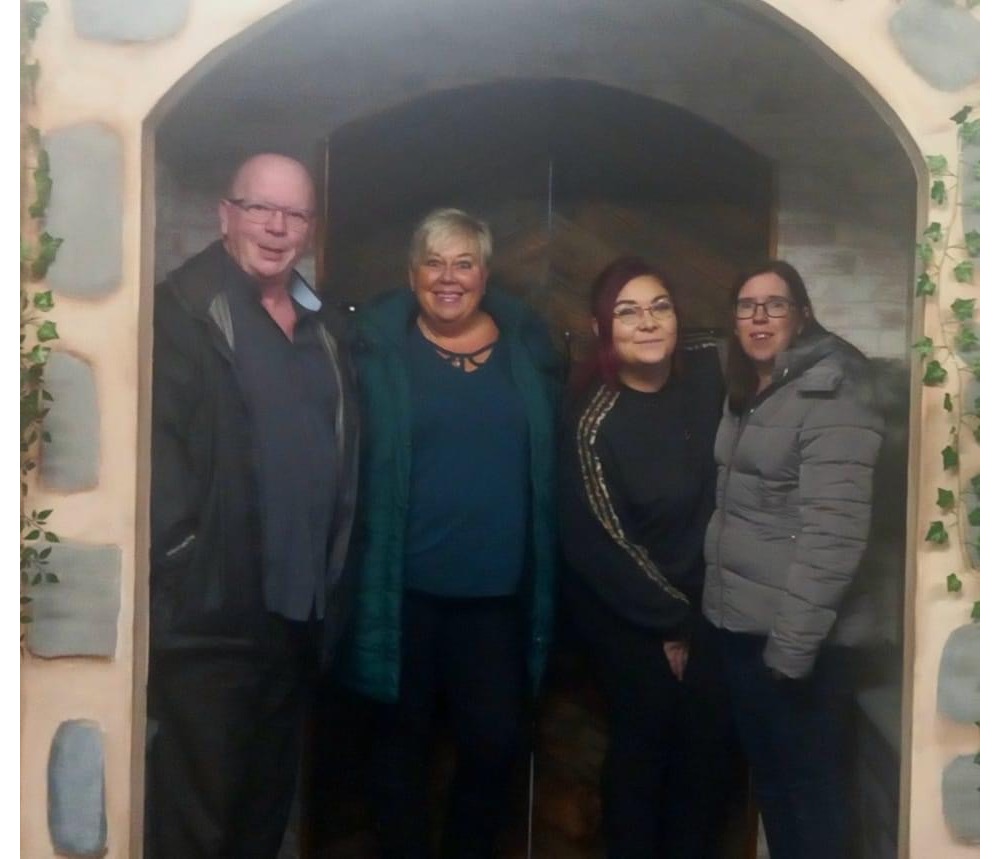 From left to right, Stuart, Dawn, Siobhan, and Helen stand smiling in the doorway of the escape room. 