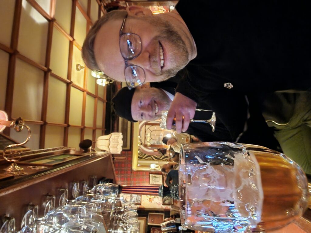 David Atkins and Jonas Bolinder sit at a cosy bar. David sits in the foreground, Jonas sits behind him raising a glass. 