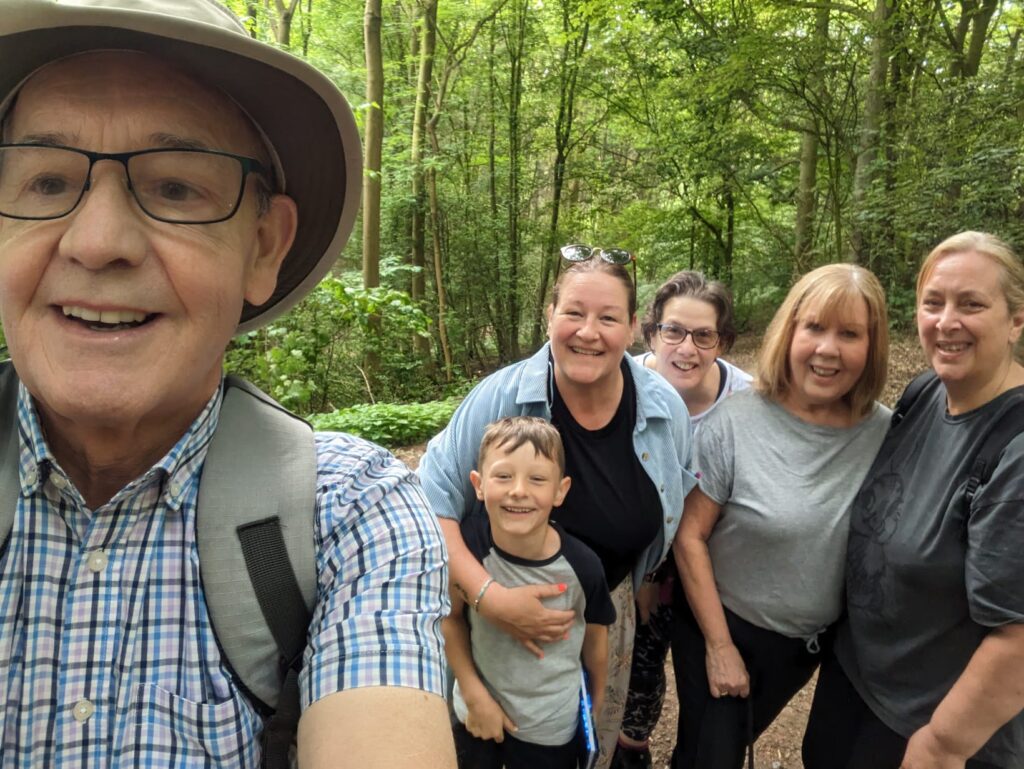The walking club stand for a selfie in a green, sunlit forest. 