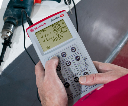 A Seaward PrimeTest 250+ PAT Tester is being used to test an electric drill. The screen indicates the drill has passed. 