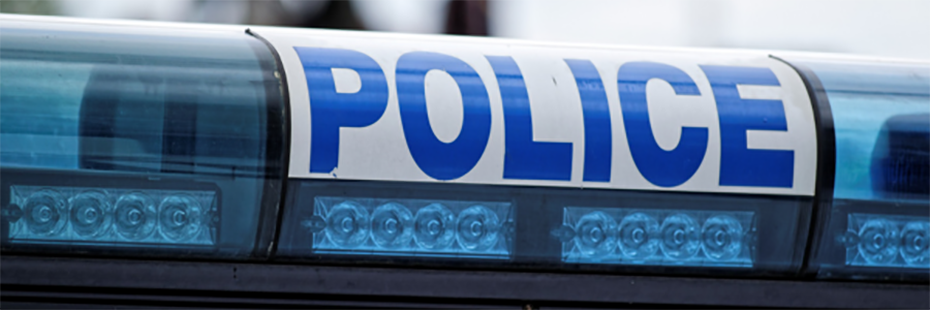 Close up image of the blue lights on top of a police vehicle. In the centre the word "POLICE" is written in blue, capital letters on a white background. 