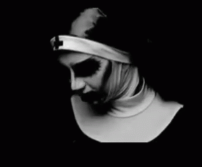 Black and white GIF of a nun-nurse slowly turning to face the camera. Her eyes are dark and her mouth is dripping with blood. 