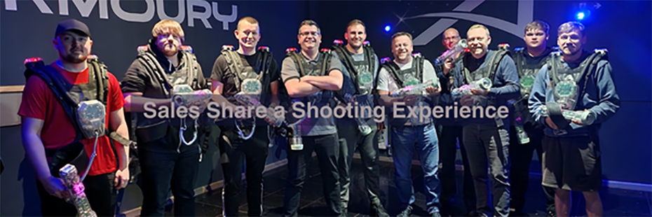 Dressed in harnesses and holding sci-fi style, transparent guns, the Sales team stand in a semi-circle smiling at the camera.  In the middle of the image, large grey text reads "Sales Share a Shooting Experience".