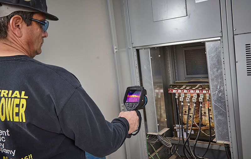 A man in a white hardhat uses a FLIR E76 to inspect an electrical panel