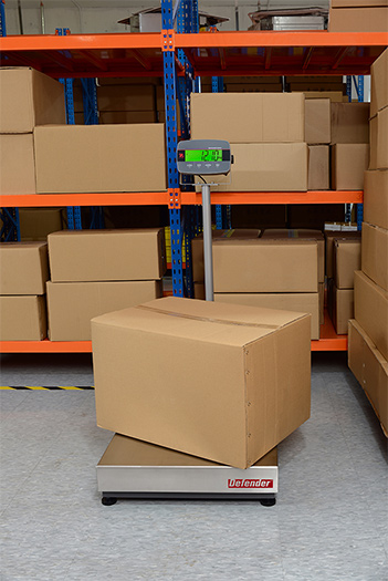 Ohaus Defender 3000 weighing a package in a warehouse environment.