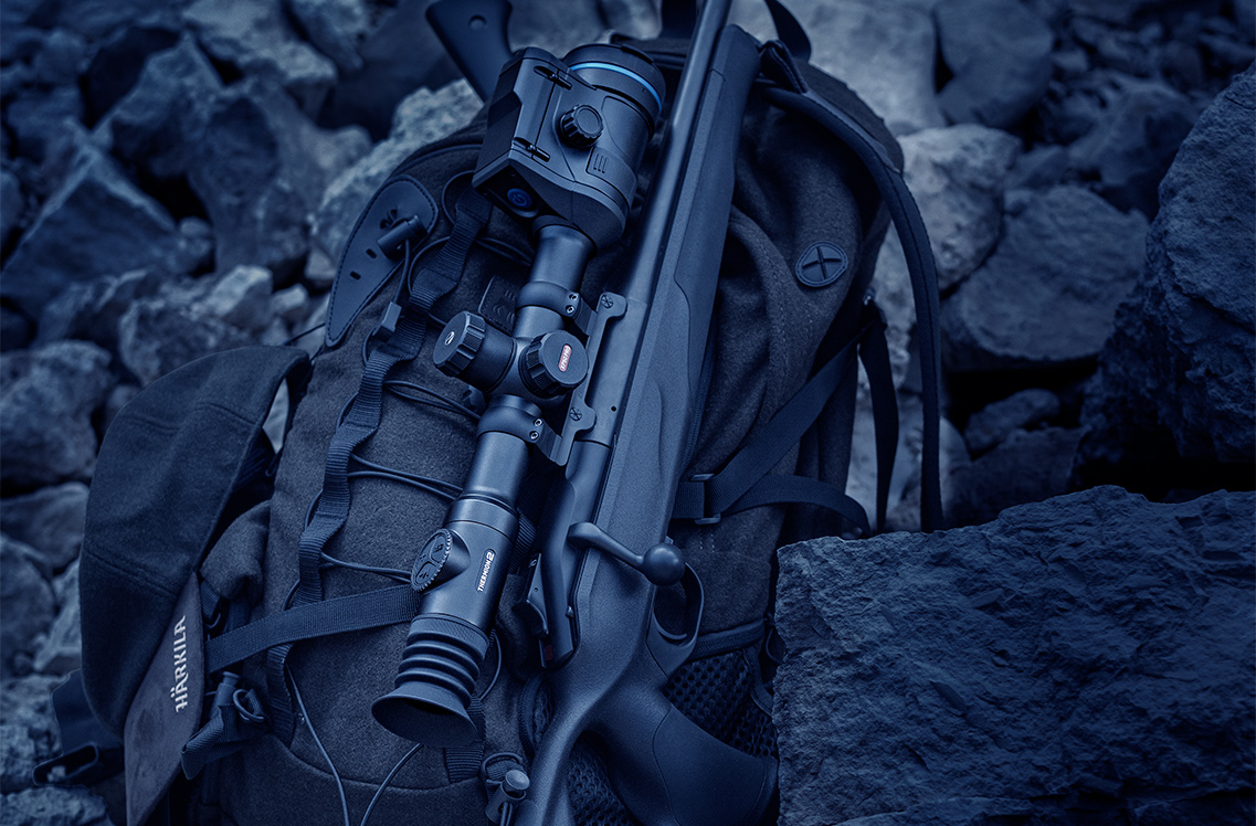 Pulsar Thermion 2 LRF XG50 Thermal Imaging Riflescope laid on a bag while attached to a gun, rocky background.